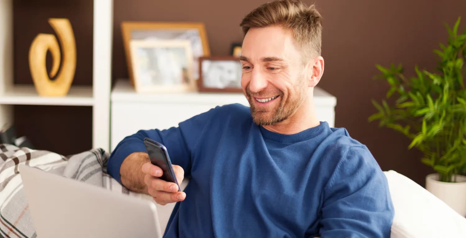 Persona sonriendo con una computadora y un celular